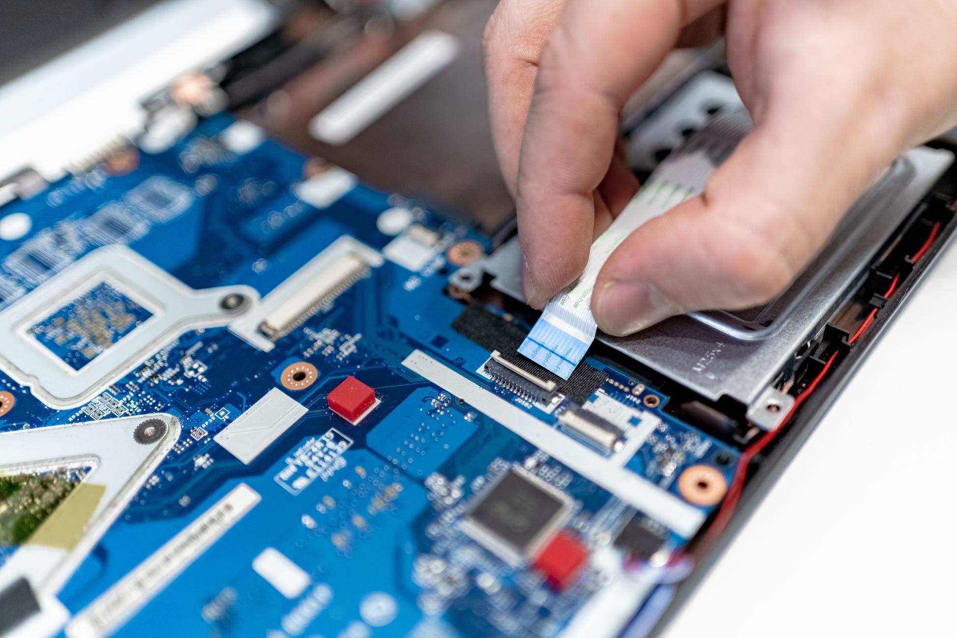 Dłonie naprawiające płytę główną laptopa z widocznymi szczegółami elektroniki